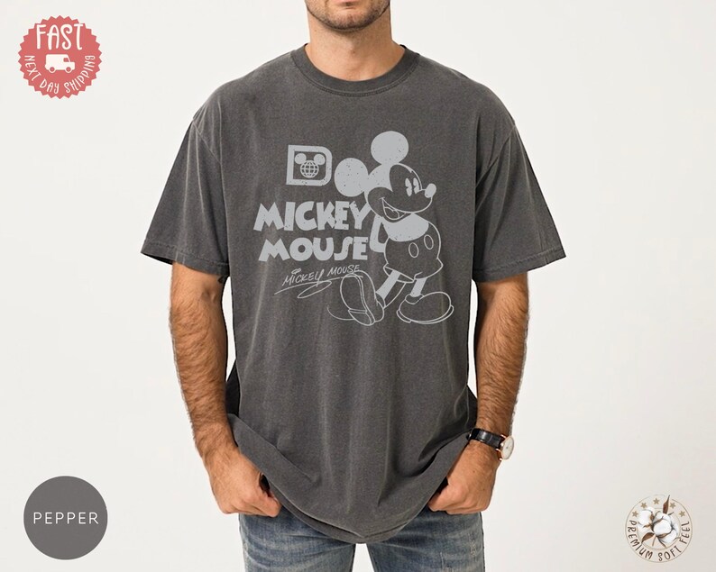 May include: Dark grey t-shirt with a distressed Mickey Mouse graphic. The design includes the words "Mickey Mouse" and Mickey's signature. The shirt has a vintage, worn appearance.