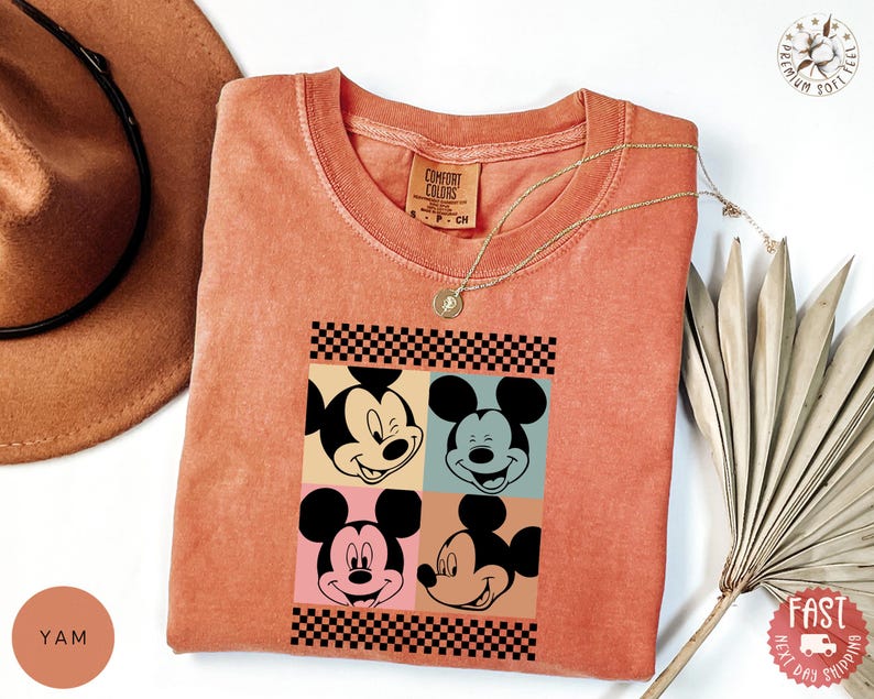Peut inclure: T-shirt corail Comfort Colors avec un motif pop art de Mickey Mouse en quatre expressions diff&eacute;rentes, encadr&eacute; d'un motif &agrave; carreaux noir et blanc. Un collier dor&eacute; est pos&eacute; sur le t-shirt. Le t-shirt a une &eacute;tiquette Comfort Colors.