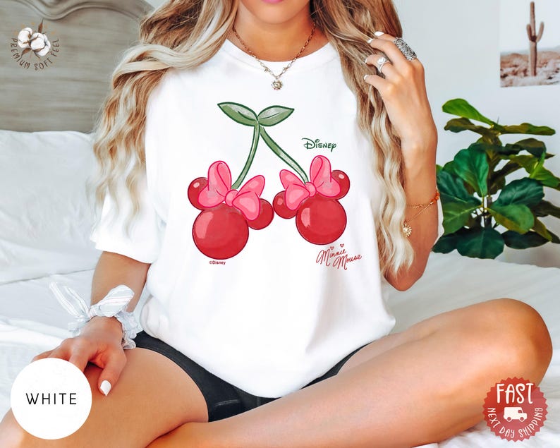 Peut inclure: T-shirt blanc avec un motif de cerises Minnie Mouse. Le graphisme comprend deux cerises rouges avec des n&oelig;uds roses, des tiges vertes et les logos Disney et Minnie Mouse. Le t-shirt est en mati&egrave;re douce.