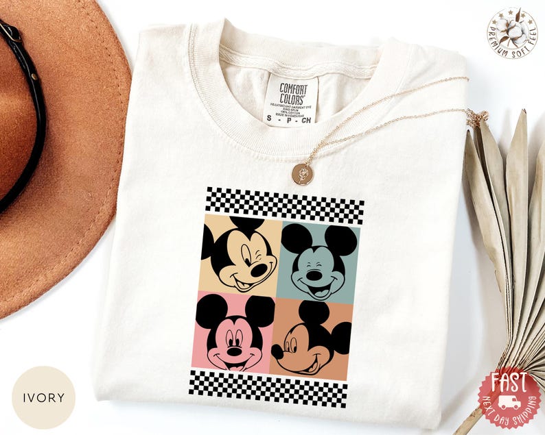 Peut inclure: T-shirt ivoire avec un motif de style pop art du visage de Mickey Mouse en quatre blocs de couleurs diff&eacute;rents. Le motif est encadr&eacute; d'un motif &agrave; carreaux noir et blanc. Col rond et manches courtes.