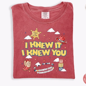 May include: A red short-sleeved t-shirt featuring the yellow text I KNEW IT I KNEW YOU. Graphics include a sheriff star with INFINITY AND BEYOND, a red cowboy hat, red cowboy boots, a beaded bracelet with YOU'VE GOT A FRIEND IN ME, and blocks.