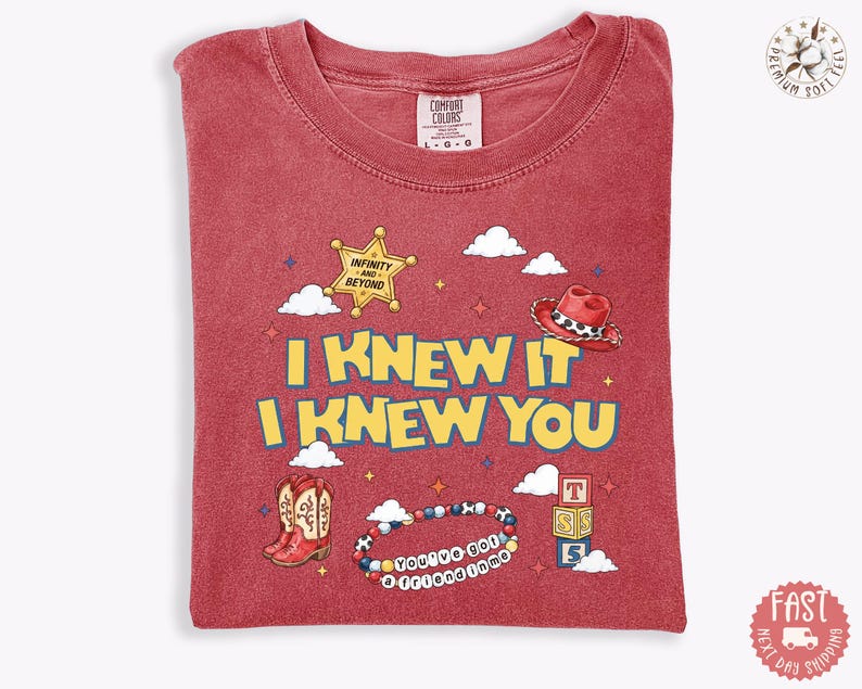 May include: A red short-sleeved t-shirt featuring the yellow text I KNEW IT I KNEW YOU. Graphics include a sheriff star with INFINITY AND BEYOND, a red cowboy hat, red cowboy boots, a beaded bracelet with YOU'VE GOT A FRIEND IN ME, and blocks.