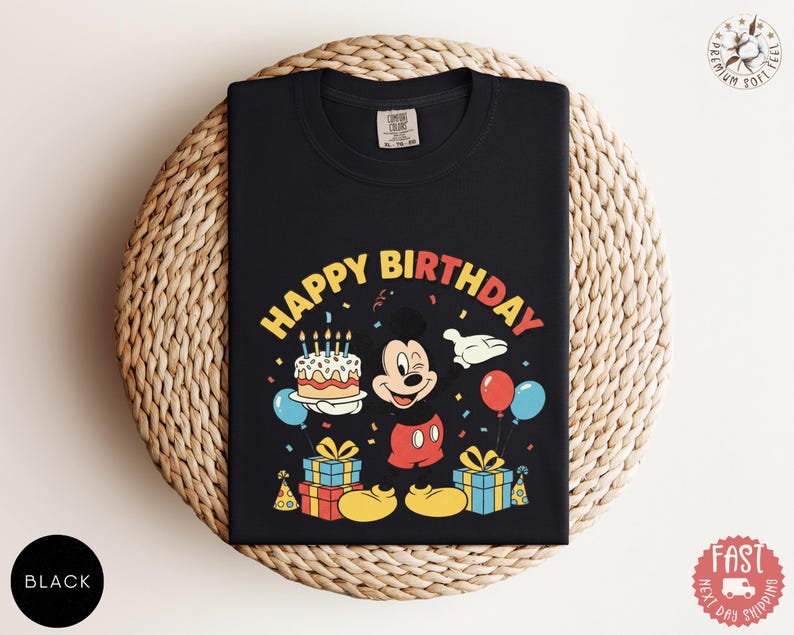 K&ouml;nnte beinhalten: Schwarzes T-Shirt mit einer farbenfrohen Grafik von Mickey Mouse, einer Geburtstagstorte, Luftballons und dem Schriftzug "HAPPY BIRTHDAY". Das Design umfasst Geschenkboxen und Konfetti und schafft ein festliches Geburtstagsthema.