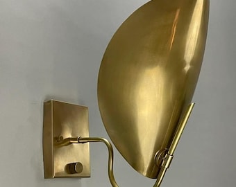 May include: A brass wall sconce with a curved, half-circle shade. The sconce has a simple, minimalist design and is perfect for adding a touch of modern style to any room.