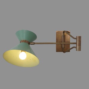 Op de afbeelding: Een messing wandlamp met een groene en gele metalen kap. De lamp heeft een zwenkarm en een rechthoekige basis.