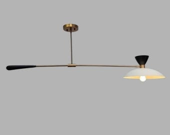 May include: A modern, minimalist ceiling light fixture. It features a long, horizontal arm with a black handle on one end and a white, bowl-shaped shade with a light bulb on the other. The fixture has brass and black accents.