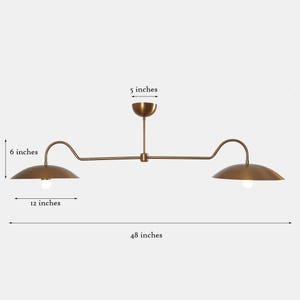 May include: A brass double-headed pendant light fixture with two curved arms. Each arm has a 6-inch diameter shade and the fixture is 48 inches long.