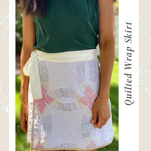 May include: A white quilted wrap skirt with a patchwork design featuring pink and yellow accents. The skirt has a white waistband and a tie closure. The image also includes the text "Quilted Wrap Skirt" and "Pattern".