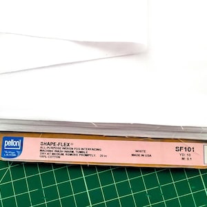 May include: A white Pellon Shape-Flex All-Purpose Woven Fus Interfacing label with the text "SHAPE-FLEX® All-Purpose Woven Fus Interfacing Machine Wash Warm, Tumble Dry at Medium, Remove Promptly. 20 in 100% Cotton" and "White Made in USA" and "SF101 YD: 10 M: 9.1".