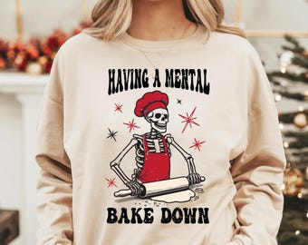 May include: A beige sweatshirt with the text "Having a mental bake down" and a skeleton wearing a chef's hat and red apron rolling out dough with a rolling pin.