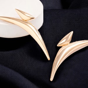 May include: A pair of gold-toned abstract earrings with a curved, wing-like design.