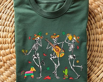 May include: Green t-shirt with a graphic of three skeletons playing music and dancing. The skeletons are wearing sombreros and holding musical instruments.