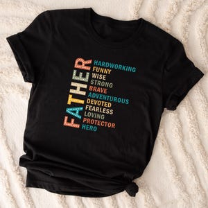 May include: Black t-shirt with the word "Father" spelled vertically in a colorful retro font. The word is surrounded by a list of positive adjectives describing a father, including "hardworking", "funny", "wise", "strong", "brave", "adventurous", "devoted", "fearless", "loving", "protector", and "hero".