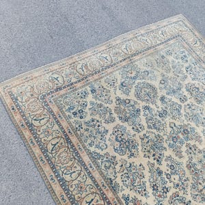 May include: An antique area rug with a cream-colored background and intricate floral patterns in shades of blue, brown, and beige. The rug features a detailed border design and a distressed, vintage appearance.