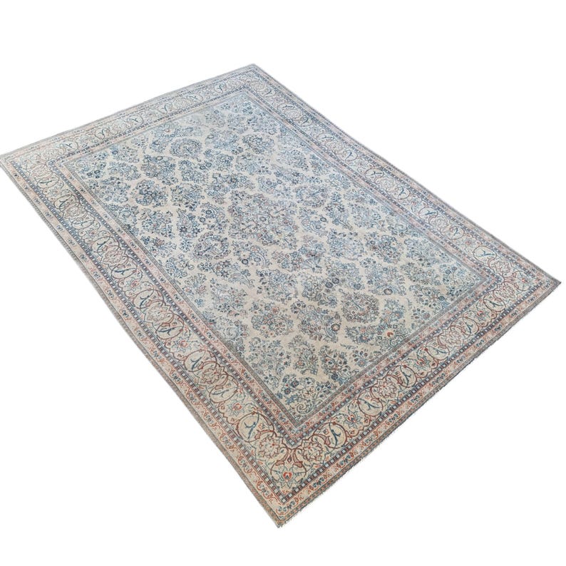 May include: An antique area rug with a cream-colored field and an intricate floral pattern in shades of blue, red, and beige. The rug features a detailed border with a repeating design. The rug is rectangular and appears to be made of woven material.