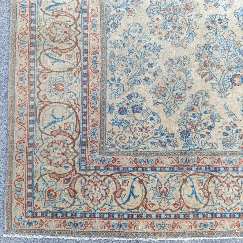 May include: Close-up of a beige rug with a detailed floral pattern in blue and red. The rug features a border with intricate designs and a central field with floral motifs, showcasing a vintage aesthetic.