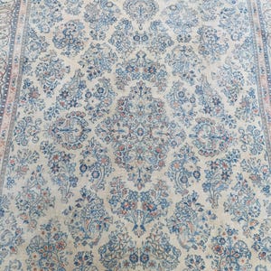 May include: Cream-colored area rug with an intricate floral pattern in shades of blue and coral. The rug features a central medallion design and a detailed border, suitable for living rooms or bedrooms.