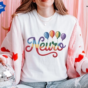 May include: White sweatshirt with the embroidered word "Neuro" in rainbow colors, accompanied by colorful balloon graphics. The sweatshirt is worn with a pink and white cardigan with red heart patterns.