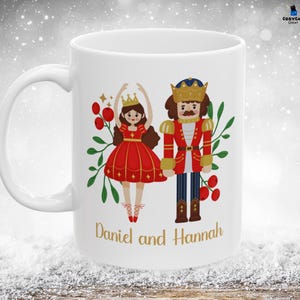 May include: White ceramic mug with a colorful illustration of a Nutcracker and a ballerina. The mug has the text "Daniel and Hannah" printed on the front.