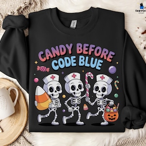 May include: Black sweatshirt with the text "CANDY BEFORE CODE BLUE" in colorful letters. The design features three skeleton nurses carrying candy and a jack-o'-lantern basket. The design includes candy corn, a candy cane, and other sweets.