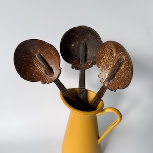 Puede incluir: Una taza de cerámica blanca con un asa negra y el texto "But First, Coffee" en negro, con una fuente de estilo manuscrito. La taza está sobre una superficie blanca.