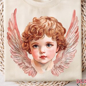 Op de afbeelding: Een cr&egrave;mekleurige trui met een vintage-illustratie van een cherubijn met roze vleugels. De cherubijn heeft krullend blond haar en draagt een witte kleding.