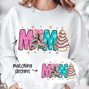 May include: White sweatshirt with the word "MAMA" in pink, blue, and green with a Christmas tree design. The word "MINA" is shown in a smaller size in the bottom right corner of the image.