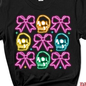 May include: Black t-shirt with a neon design of colorful skulls and bows. The skulls are outlined in neon yellow, green, pink, and blue. The bows are pink, yellow, and green.