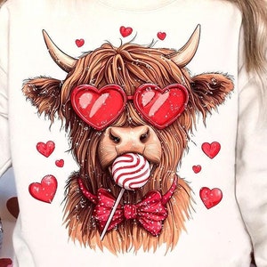 May include: A white sweatshirt with a brown and white Highland cow wearing red heart-shaped sunglasses and a red bow tie. The cow is holding a red and white lollipop.