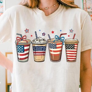 May include: White t-shirt with a graphic of four iced coffee cups decorated with the American flag.