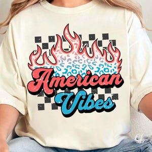May include: A white t-shirt with a graphic of a flame with a leopard print design. The text "American Vibes" is written in a retro font below the flame.