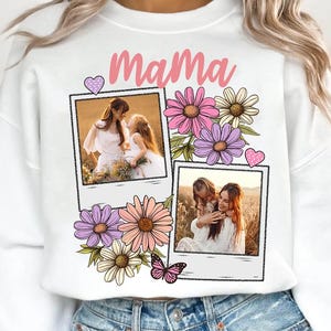 May include: White sweatshirt with the word "Mama" in pink script, decorated with floral graphics and two framed photos. The photos show a mother and child. A butterfly and heart accents complete the design.