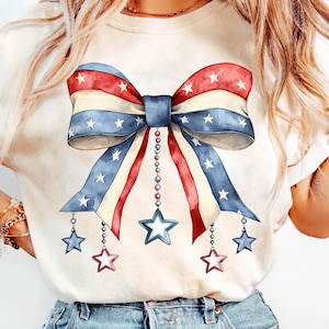 May include: A white t-shirt with a red, white, and blue bow with stars. The bow has a string of beads hanging from it with stars at the end of each string.