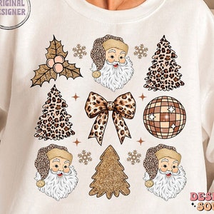 May include: White sweatshirt with a Christmas design featuring Santa Claus, a leopard print Christmas tree, a gold glitter Christmas tree, a disco ball, a bow, and holly. The text "Design Soul" is printed on the bottom right corner of the sweatshirt.