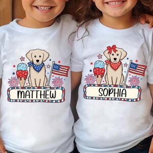 Pu&ograve; includere: Due magliette bianche a tema patriottico. Una maglietta presenta un cane giallo con una bandana rosso, bianco e blu, un cono gelato, fuochi d'artificio e il nome "MATTHEW". L'altra maglietta presenta un cane giallo con un fiocco rosso, un cono gelato, fuochi d'artificio e il nome "SOPHIA".