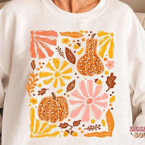 May include: White sweatshirt with a graphic print of a square filled with orange, yellow, pink, and brown floral and pumpkin designs. The text "DESIGN SOUL" is printed in the bottom right corner.