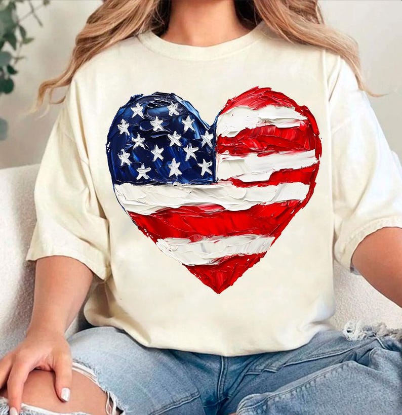 Pu&ograve; includere: Una maglietta bianca con un design dipinto a forma di cuore della bandiera americana. La bandiera &egrave; rossa, bianca e blu con un effetto a pennellate.