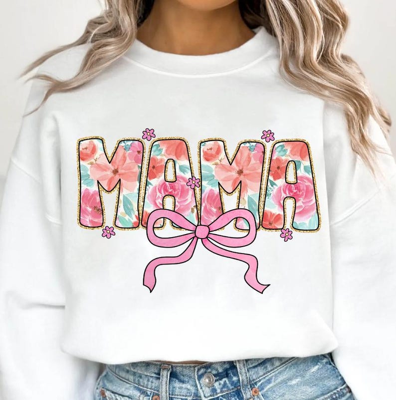 May include: White sweatshirt with the word "MAMA" in pink and gold letters with a floral pattern. The letters are outlined in gold and have a pink bow underneath.