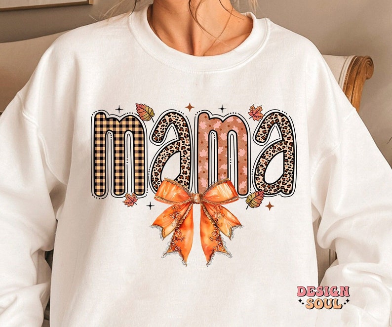 May include: White sweatshirt with the word "mama" in a fall-themed font with a plaid, leopard print, and leaf pattern. A large orange bow is below the word.