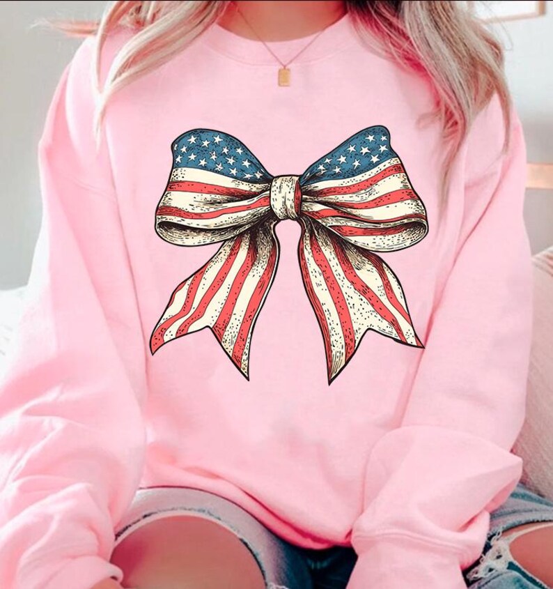 Peut inclure: Un sweat-shirt rose avec un grand n&oelig;ud rouge, blanc et bleu imprim&eacute; sur le devant. Le n&oelig;ud est dans le style du drapeau am&eacute;ricain.