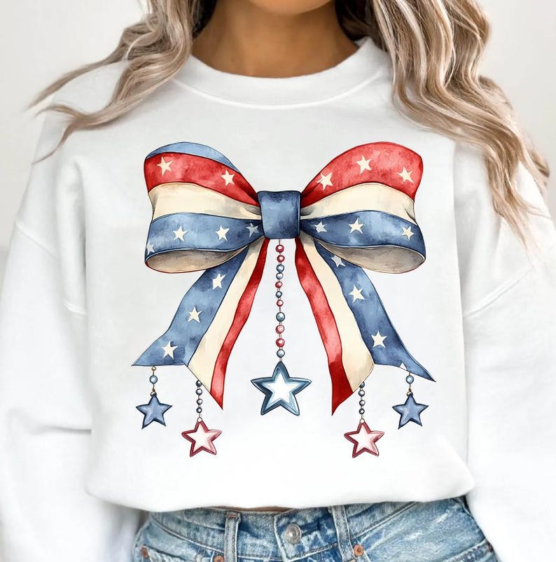 May include: White sweatshirt with a red, white, and blue bow with stars printed on it. The bow has strings with stars hanging from it.