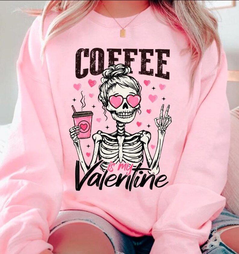 May include: Pink sweatshirt with a skeleton wearing heart-shaped sunglasses and holding a coffee cup. The text "COFFEE is my VALENTINE" is printed on the sweatshirt.