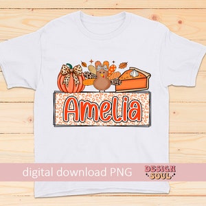May include: White t-shirt with a Thanksgiving-themed design featuring a pumpkin, a turkey, and a slice of pie. The design is surrounded by a leopard print frame with the name "Amelia" in orange letters.