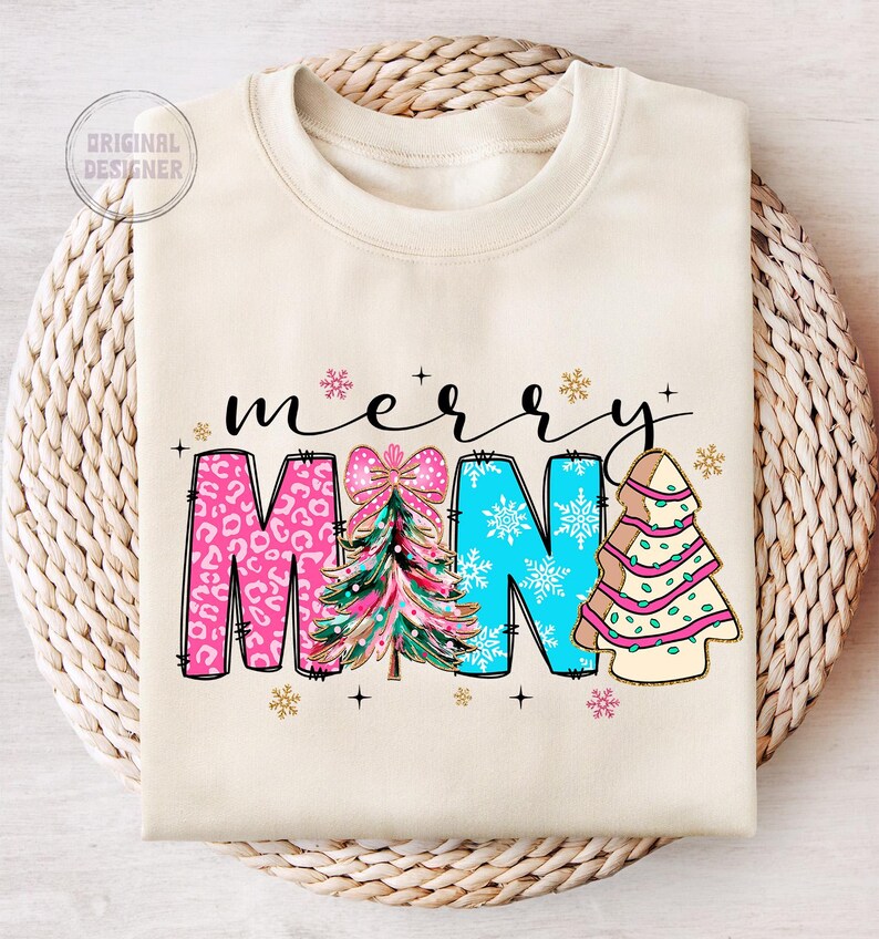 Peut inclure: Un sweat-shirt cr&egrave;me avec les mots "merry" et "mama" en lettres noires soulign&eacute;es. Les lettres sont d&eacute;cor&eacute;es de sapins de No&euml;l roses, bleus et verts et de flocons de neige.