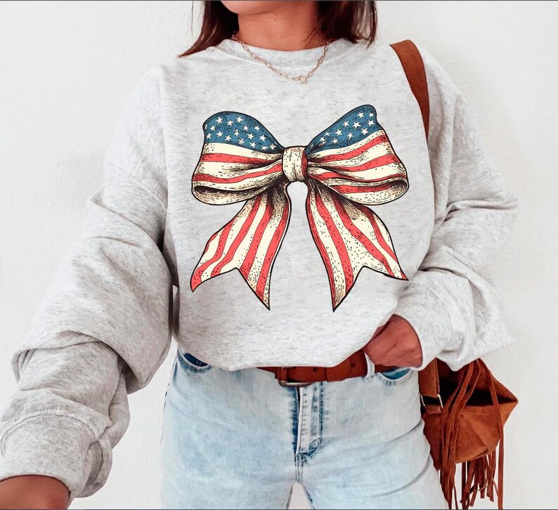 Peut inclure: Un sweat-shirt gris avec un grand n&oelig;ud rouge, blanc et bleu imprim&eacute; sur le devant. Le n&oelig;ud est dans le style du drapeau am&eacute;ricain.