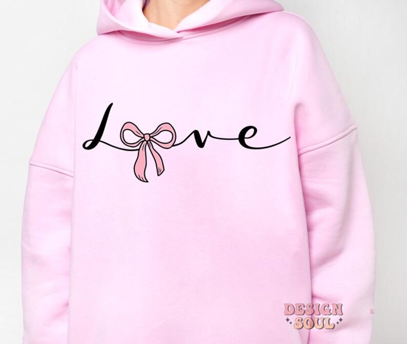 May include: Pink hoodie with a black cursive word "love" with a pink bow in the middle of the word.