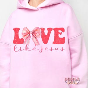 May include: Pink hoodie with the words "LOVE like JESUS" in red letters with a pink bow in the middle of the word LOVE.