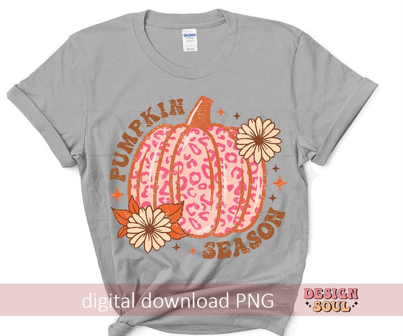May include: A gray t-shirt with the text "Pumpkin Season" in orange and brown letters. A pink and orange pumpkin with a leopard print design is in the center of the shirt. The pumpkin is surrounded by orange and yellow flowers.