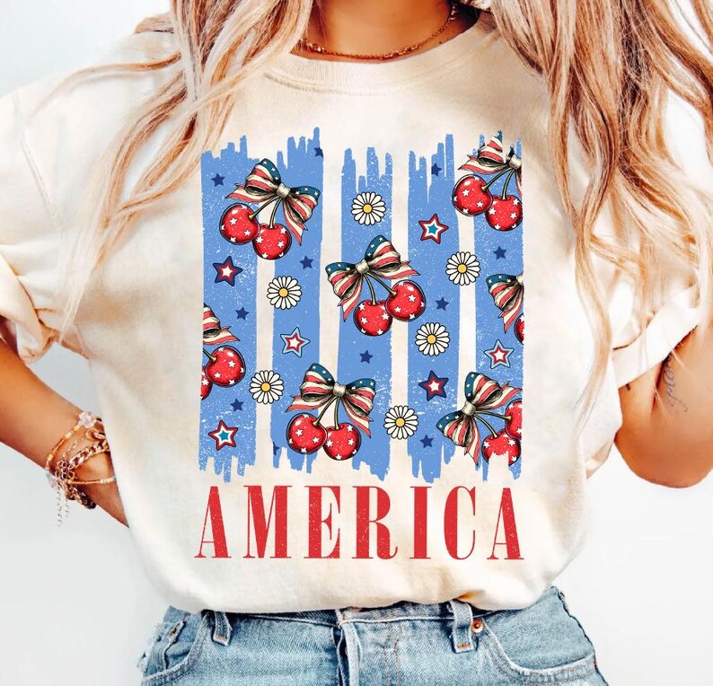 May include: A white t-shirt with a blue, red, and white graphic of cherries and stars with the word "AMERICA" printed below.