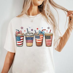 May include: White t-shirt with a graphic of four iced coffee cups decorated with the American flag.
